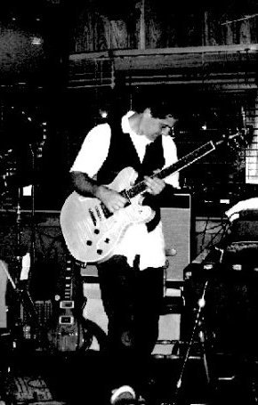 Black-and-white live shot, head bowed over a Les Paul mid-song.